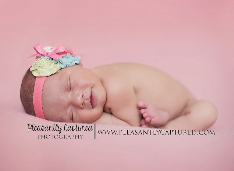 newborn girl smiling in sleep wearing bow - jacksonville wilmington new bern nc newborn baby photography