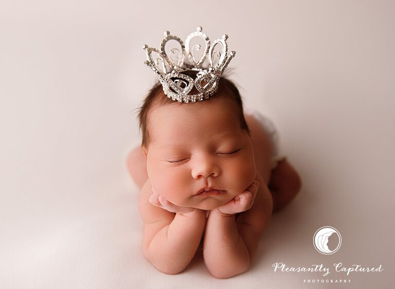 Newborn baby girl holding head in hands with crown on head - baby pictures nc