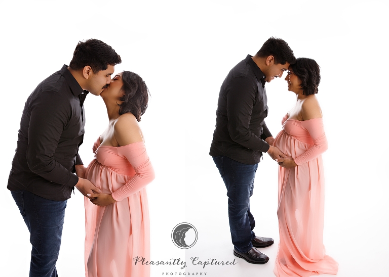 Pregnant mother wearing pink dress and smiling and kissing husband 