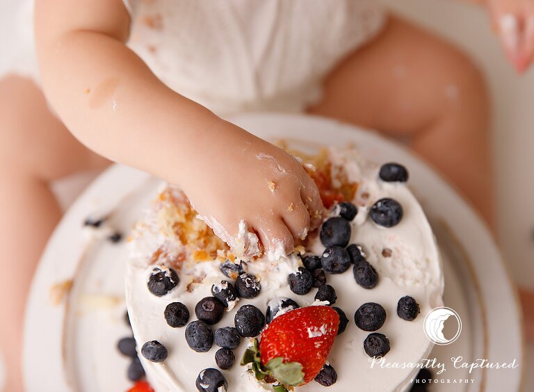 Little girl's hand grabs berries from her first birthday cake birthday photographer nc