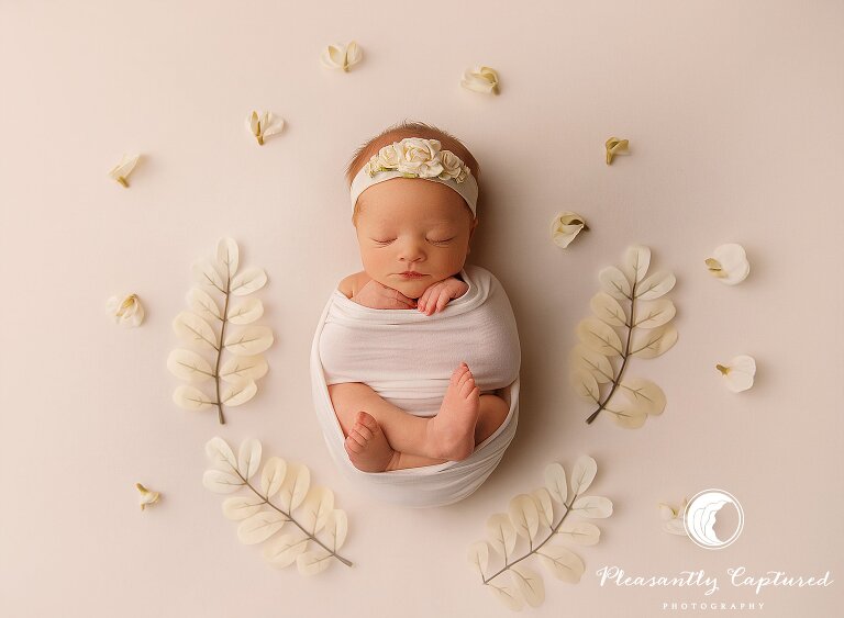 Newborn baby girl surrounded by off white flowers and leaves - Sneads Ferry Newborn Photography | New Family of 3