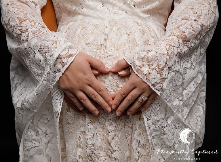 Beautiful mother to be in lace gown against bright black background making heart over belly maternity photography jacksonville nc