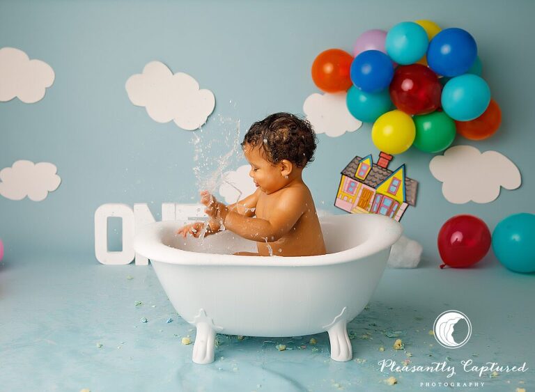 Little boy splashing water in claw foot tub during Up Themed Cake Smash | Birthday Photography Jacksonville NC