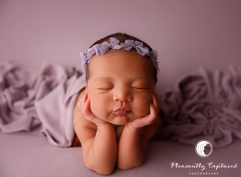 Newborn baby girl wearing purple bow headband with head on hands - richlands nc Newborn photographer