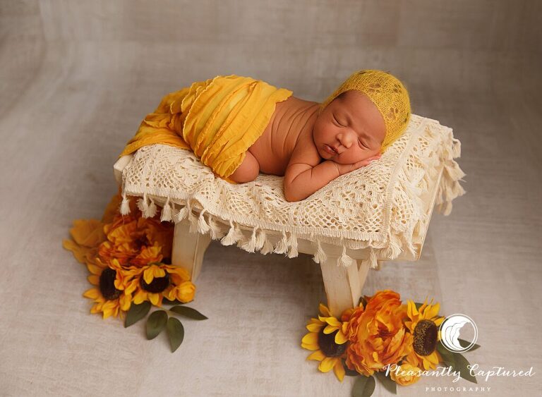 Baby girl wearing yellow bonnet, wrapped in frilly yellow fabric, laying on bench surrounded by sunflowers - richlands nc Newborn photographer