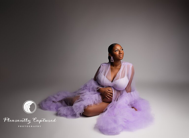 Regal studio maternity session with expecting mom in purple robe, captured in soft studio lighting