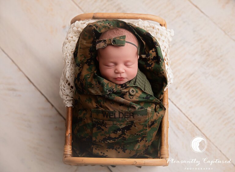 Newborn baby girl wrapped in Marine camouflage uniform with personalized name patch and bow during military-themed newborn session in Jacksonville, NC