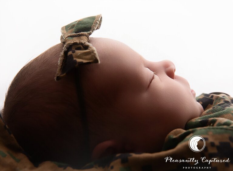 Studio newborn portrait featuring baby girl swaddled in Marine camo blouse labeled with family name