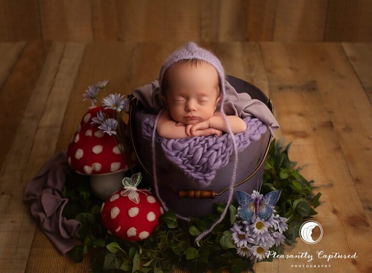 Fairy like newborn setup with baby in purple bucket with mushrooms, greenery and butterflies | newborn photographer near wilmington and newborn nc