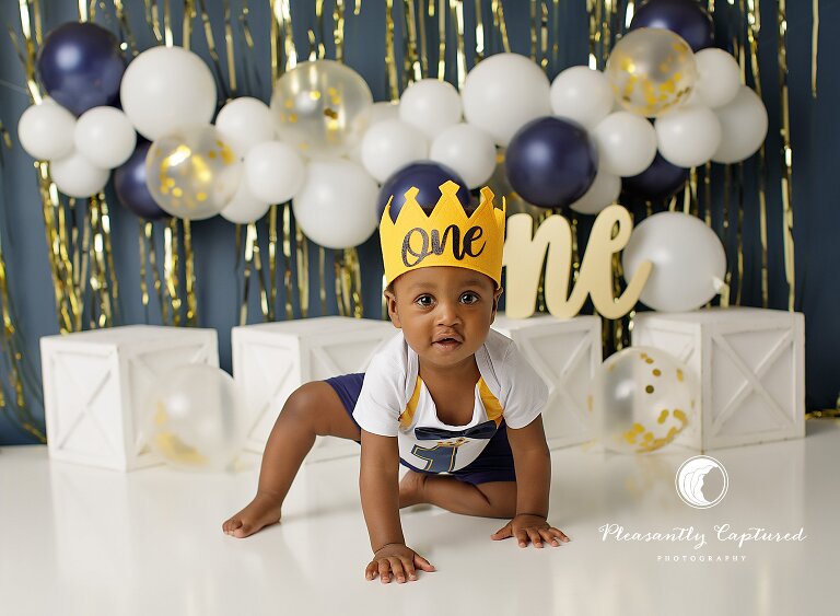 Baby boy crawling toward the camera during a playful first birthday cake smash session.