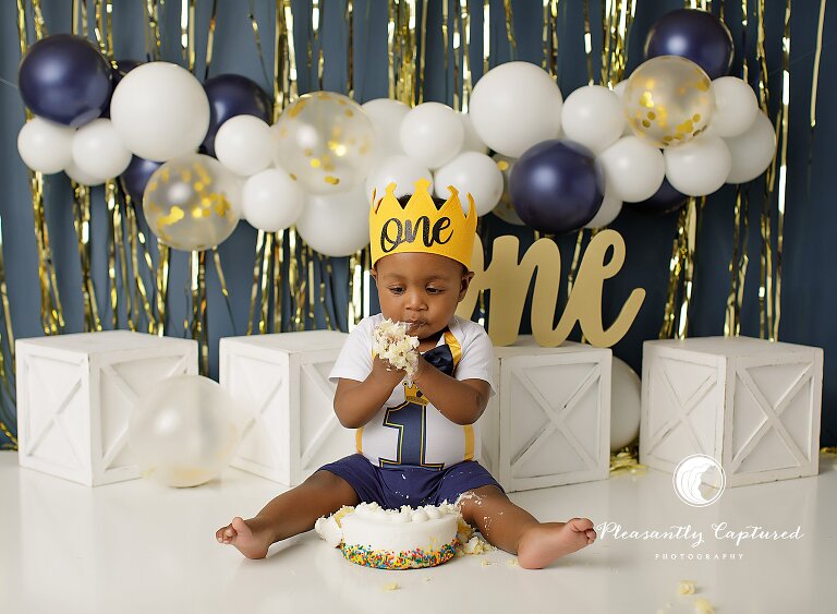 Baby boy enjoying a cake smash session with frosting-covered hands and a joyful expression.