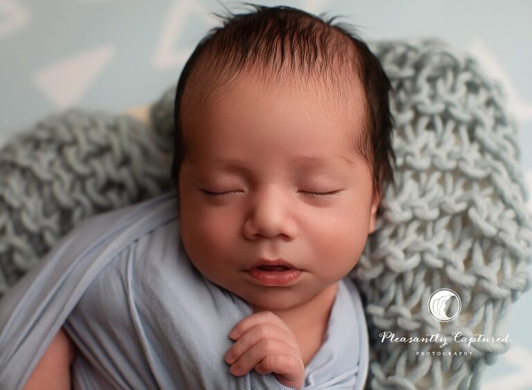 Baby boy with head full of hair wrapped in blue during studio newborn photography Jacksonville NC