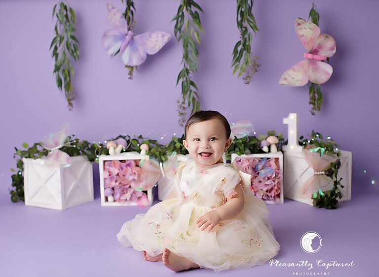 Baby girl smiling during a fairy butterfly garden cake smash session with Pleasantly Captured Photography, a cake smash photographer in Jacksonville, NC.