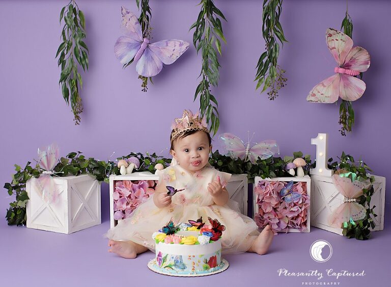 Baby girl sitting in a lavender butterfly garden setup for her first birthday cake smash session in Jacksonville, NC.