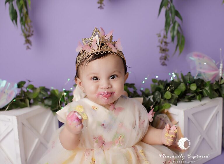 Baby girl wearing a soft embroidered dress during a fairy garden cake smash session in Jacksonville, NC.