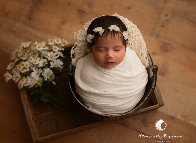 Newborn mini session in Jacksonville, NC featuring a baby girl swaddled in white with soft daisy details.
