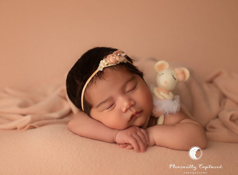 Jacksonville, NC newborn photographer capturing a baby girl in a gentle table pose with floral headband and peach styling.